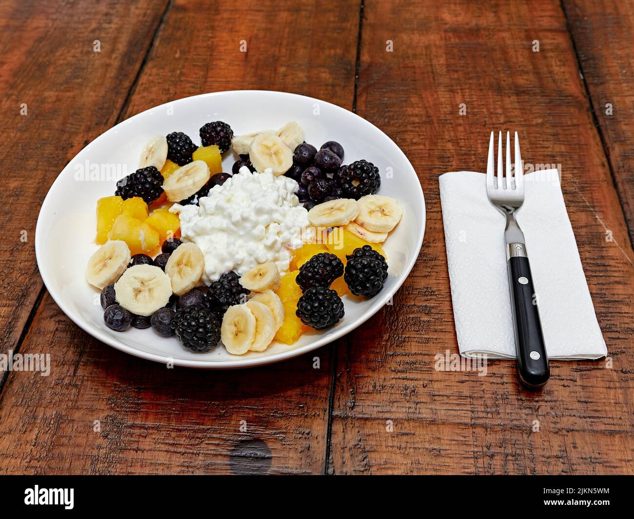 Gesunde Mahlzeit zum Frühstück oder Mittagessen Schüssel mit Quark und Obst, bestehend aus Bananenscheiben, Heidelbeeren und Brombeeren, Blick von oben. Stockfoto