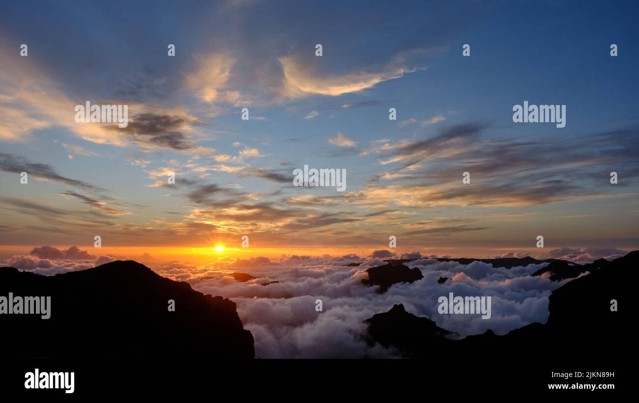 Untergehende Sonne auf und unter den Wolken während des Sonnenuntergangs. Blauer und oranger Himmel und igh Wolken und Nebel im Tal. Stockfoto