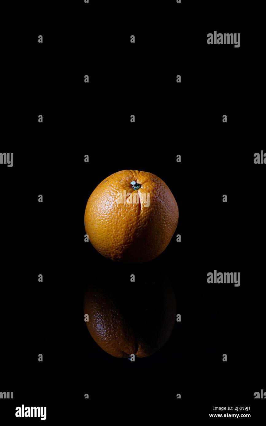 Eine vertikale Nahaufnahme einer Mandarine, isoliert auf einem schwarzen Hintergrund mit einer Reflexion Stockfoto