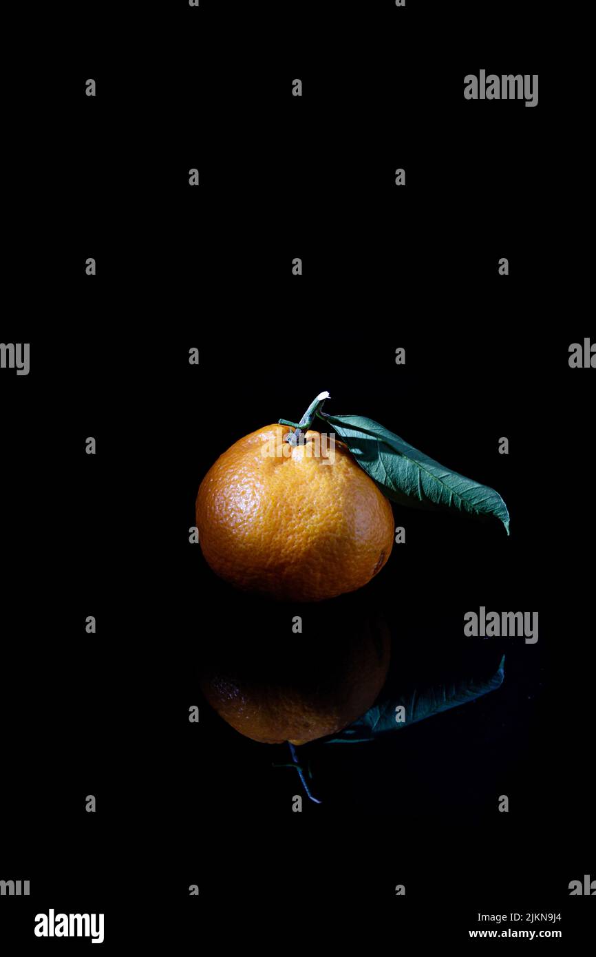 Eine vertikale Nahaufnahme einer Mandarine, isoliert auf einem schwarzen Hintergrund mit einer Reflexion Stockfoto