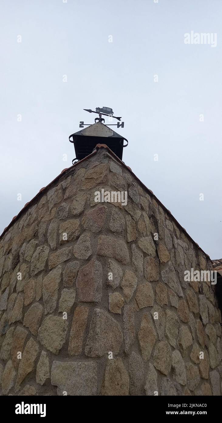 Eine vertikale Aufnahme einer Wetterfahne in Form eines Autos auf dem Dach eines alten Steinhauses gegen einen bewölkten Himmel Stockfoto