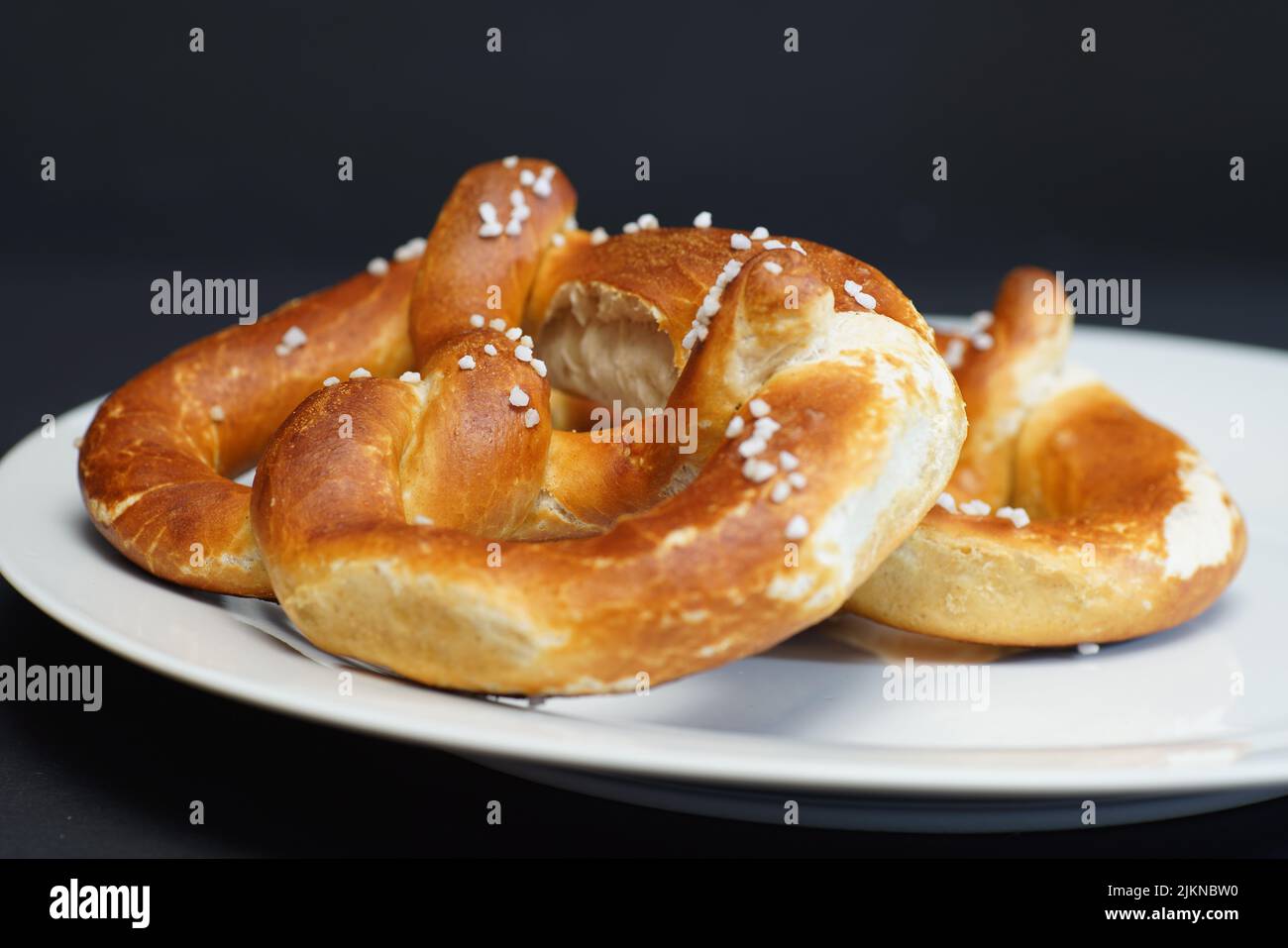 Eine Auswahl frisch gebackener, weicher Brezel auf einem weißen Teller auf grauem Hintergrund Stockfoto