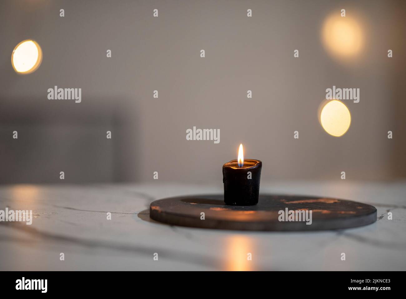 Eine Nahaufnahme einer brennenden schwarzen Kerze auf einem weißen Marmortisch auf einem unscharfen Bokeh-Hintergrund Stockfoto