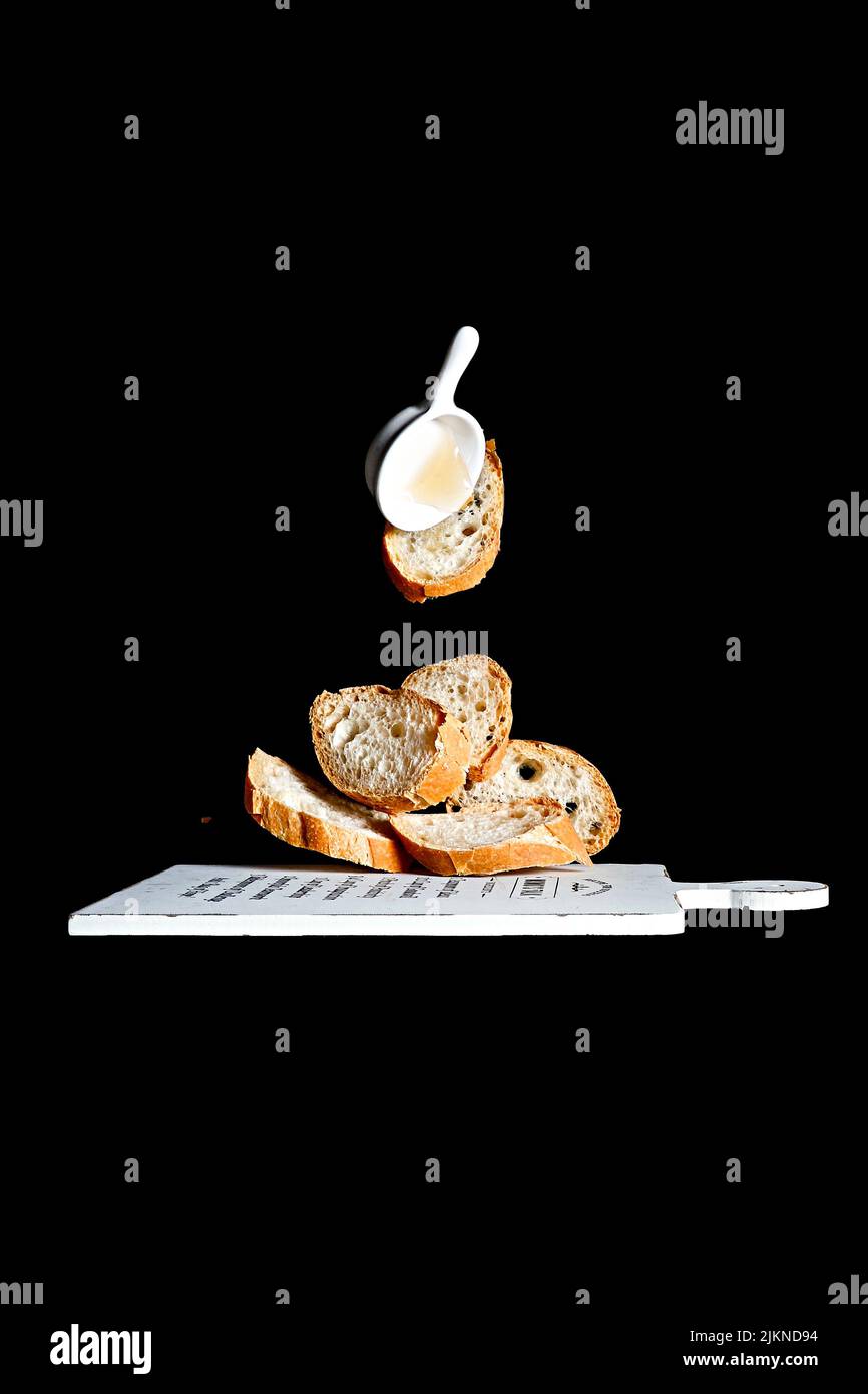 Eine vertikale Aufnahme von leckeren, gerade gebackenen Baguette-Scheiben und Sauce, die über einem hölzernen Schneidebrett schweben Stockfoto