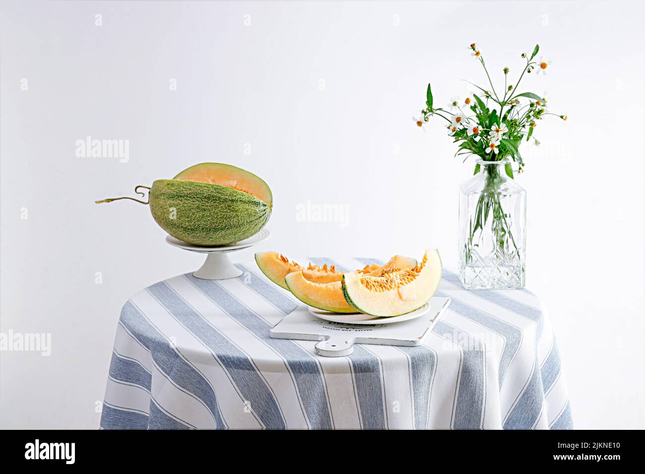 Ein Stillleben Foto von Melonenscheiben und Blumen in einer Vase auf einem runden Tisch Stockfoto