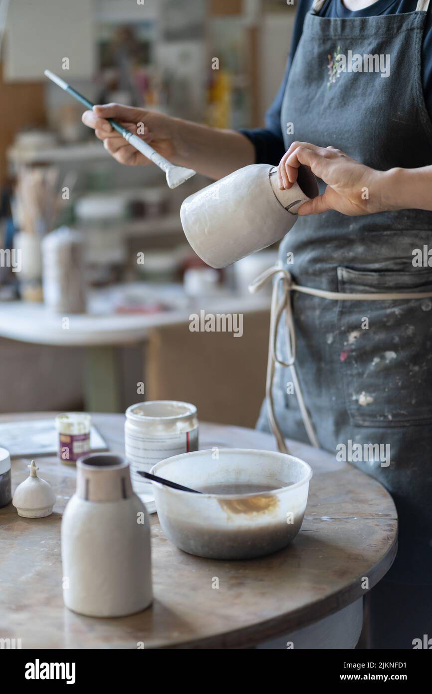 Crop Foto von Frau Handwerker Herstellung Steingut Vase Vorbereitung für die Farbe mit Pinsel Stockfoto