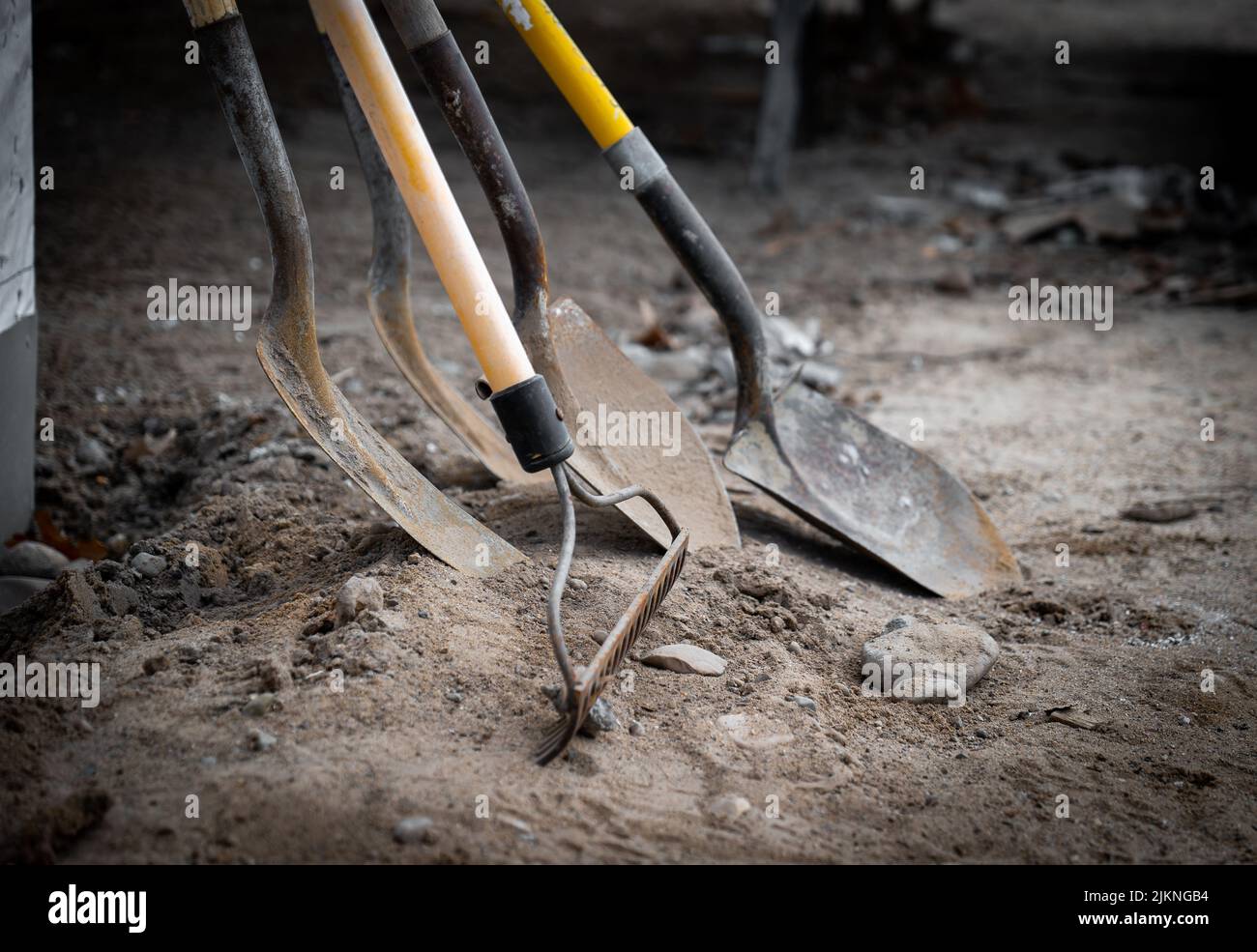 Schmutzige gebrauchte Schaufeln und ein Rechen lehnen sich während einer Arbeitspause auf einer neuen Baustelle für den Hausbau an eine Wand. Stockfoto