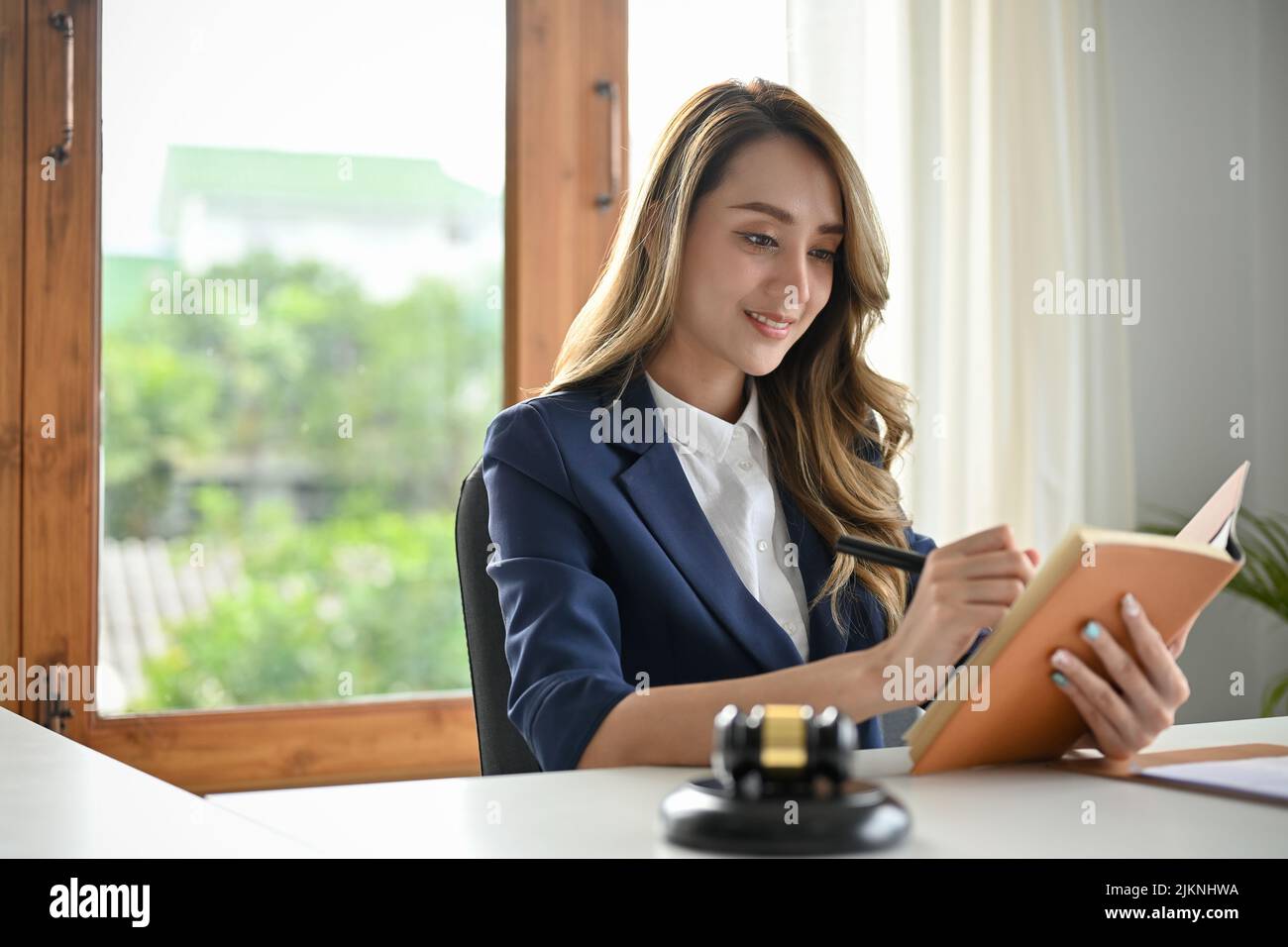 Erfolgreiche und wunderschöne junge asiatische Rechtsanwältin oder Business-Rechtsberaterin beim Lesen eines Gesetzbuches an ihrem Schreibtisch. Stockfoto
