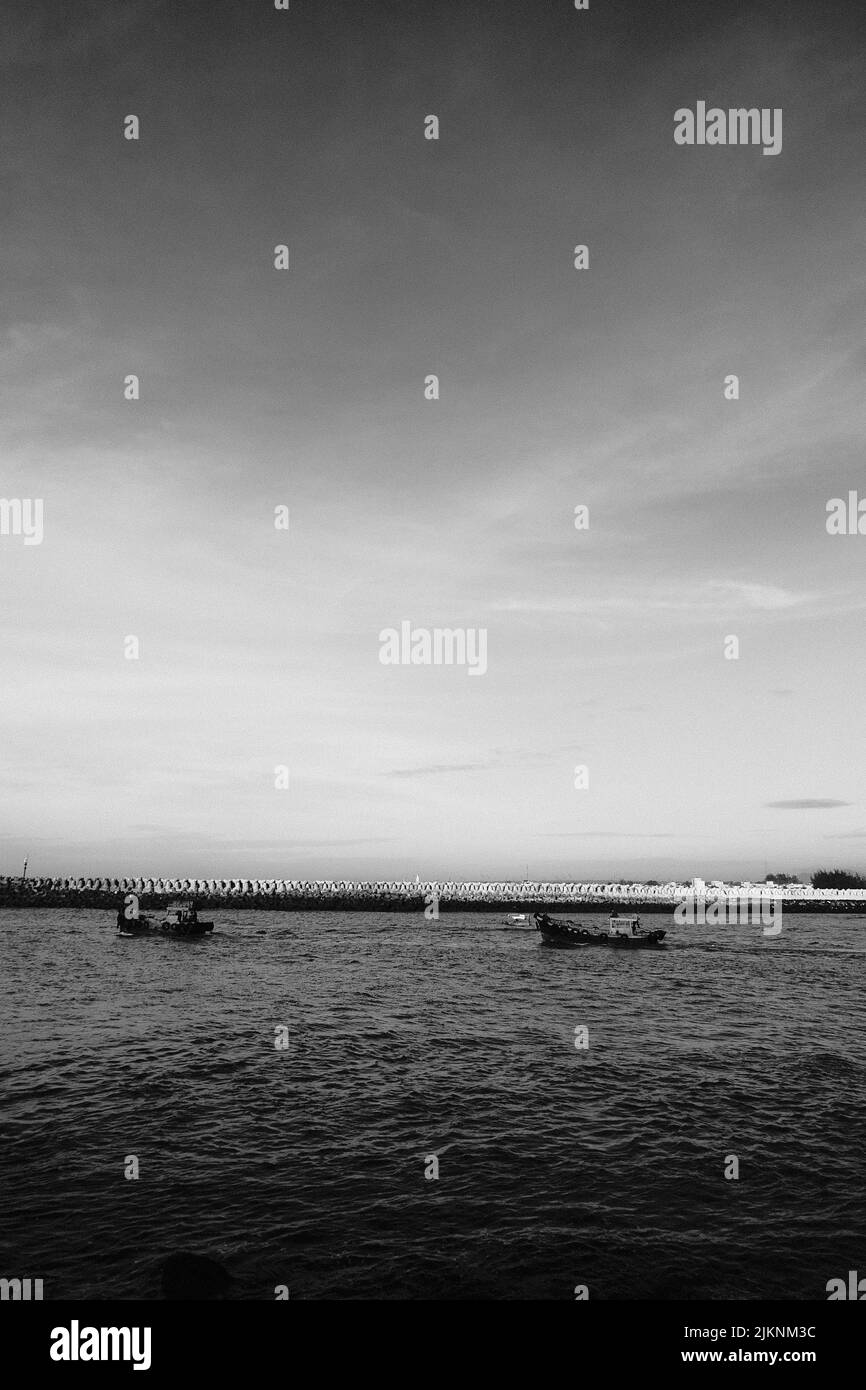 Eine vertikale Aufnahme von schwimmenden Booten im Meer in schwarz-weiß Stockfoto