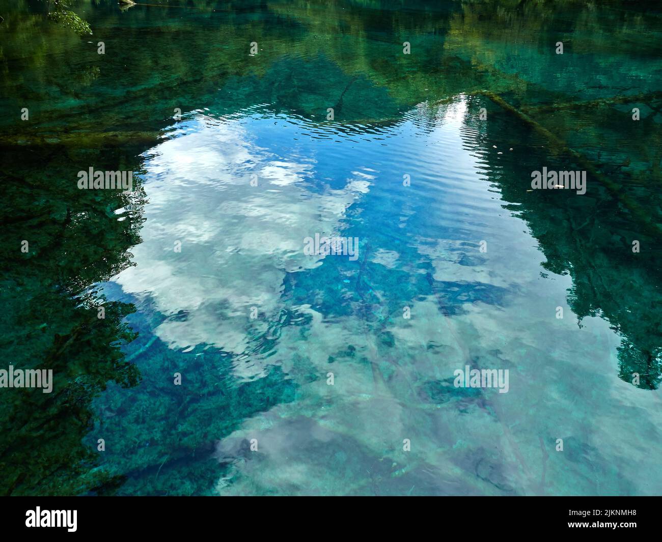 Der ruhige See mit dem Spiegelbild von grünen Bäumen und wolkig blauen Himmel in ihm Stockfoto