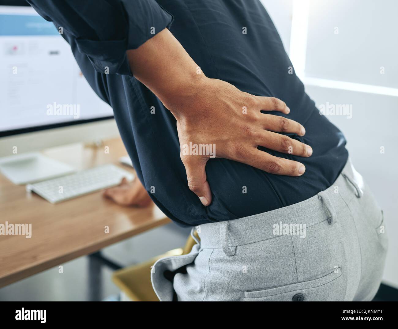 Chiropraktiker, hier komme ich. Ein nicht erkennbarer Geschäftsmann, der allein in seinem Büro steht und unter Rückenschmerzen leidet. Stockfoto