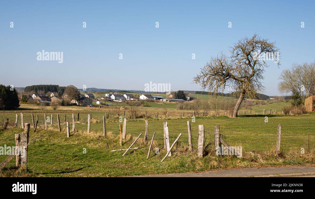 Ein Zaun auf einem Feld mit Häusern im Hintergrund in Vaux-sur-Sure, Belgien Stockfoto