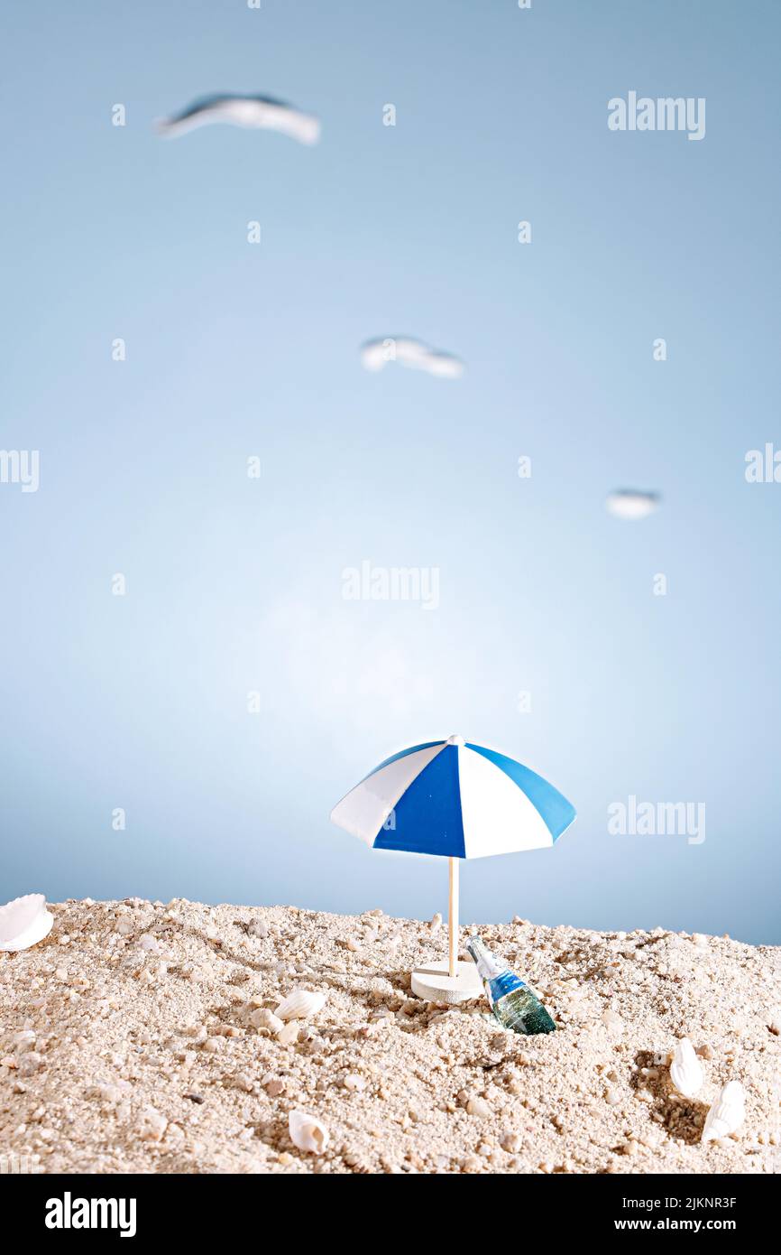 Eine vertikale Nahaufnahme einer Miniatur eines Sonnenschirms und einer Champagnerflasche am Strand - Urlaubskonzept Stockfoto