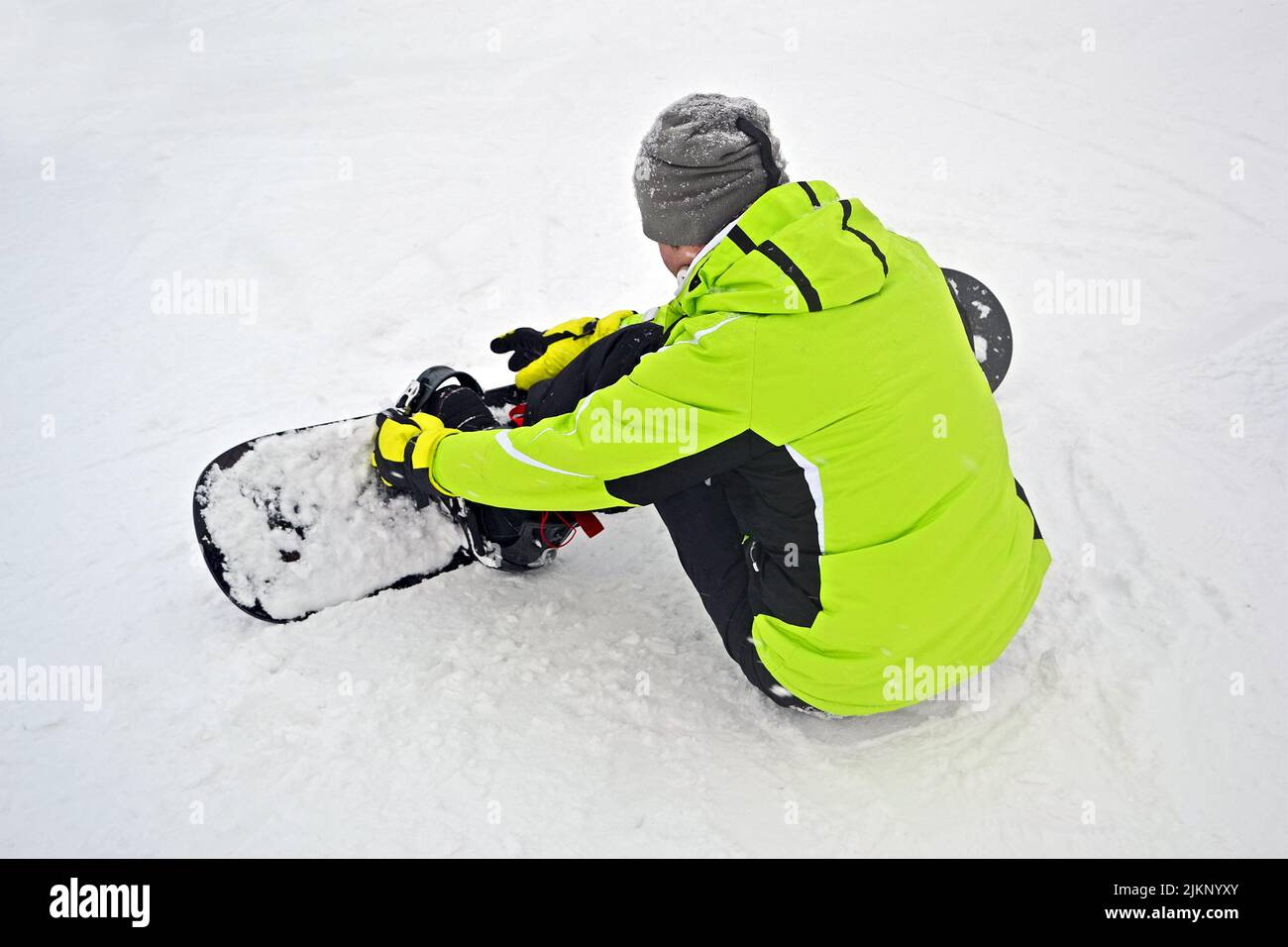 Mann mit Skateboard-Sitz auf weißem Schnee und Check-Bindung, Sport-Vielfalt Stockfoto