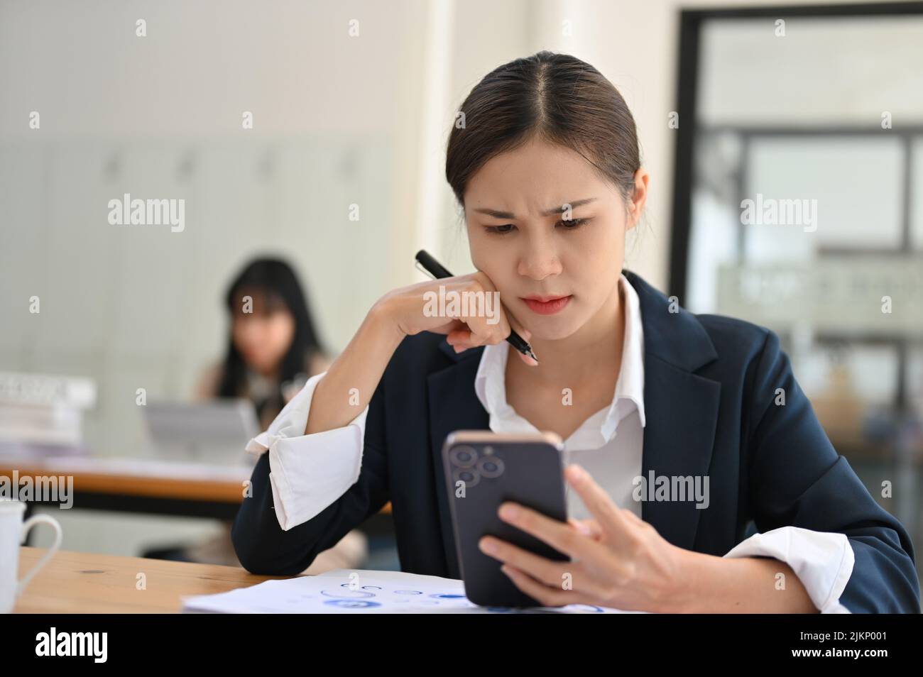 Gestresste junge asiatische Geschäftsfrau oder Büroangestellte, die ein Problem mit ihrem Smartphone hatte und eine schockierte E-Mail erhielt. Stockfoto