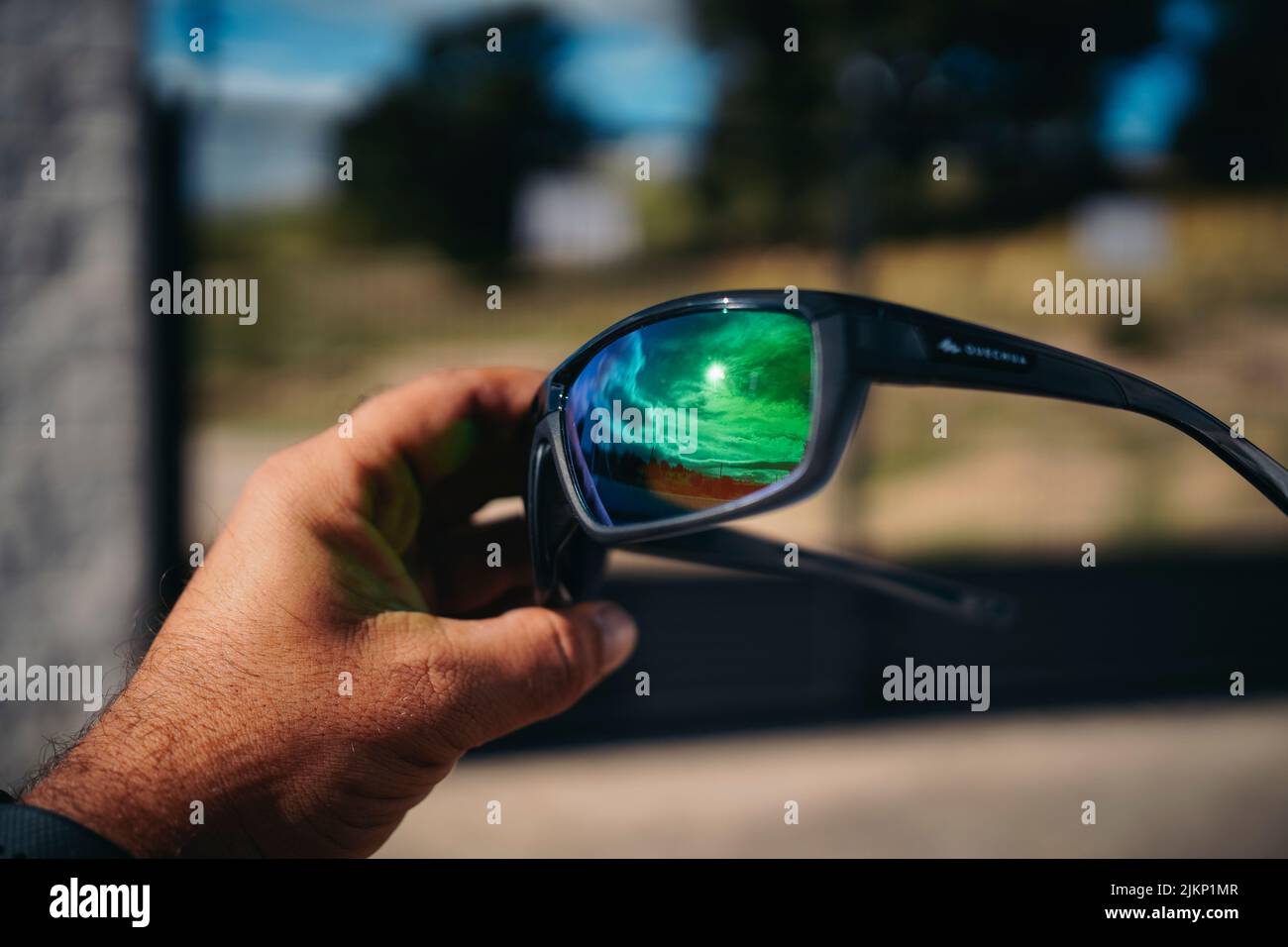 Sonnenbrille, die die Sonne reflektiert, gehalten von der Hand eines Mannes Stockfoto