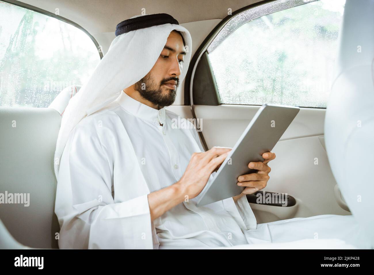 Mann mit Turban und einem Pad, während er auf seinem Auto sitzt Stockfoto