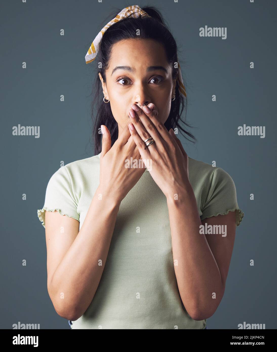 Ich bin nicht gut damit, Geheimnisse zu bewahren. Studioaufnahme einer jungen Frau, die mit ihren Händen über ihrem Mund steht. Stockfoto