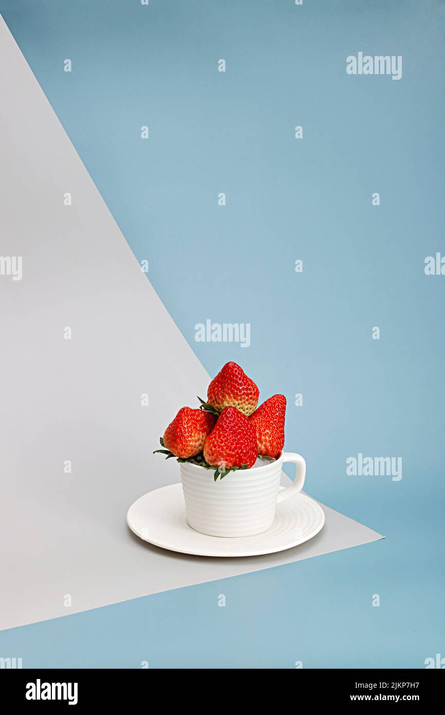Eine vertikale Komposition aus Erdbeeren in einer Tasse auf blauem Hintergrund Stockfoto