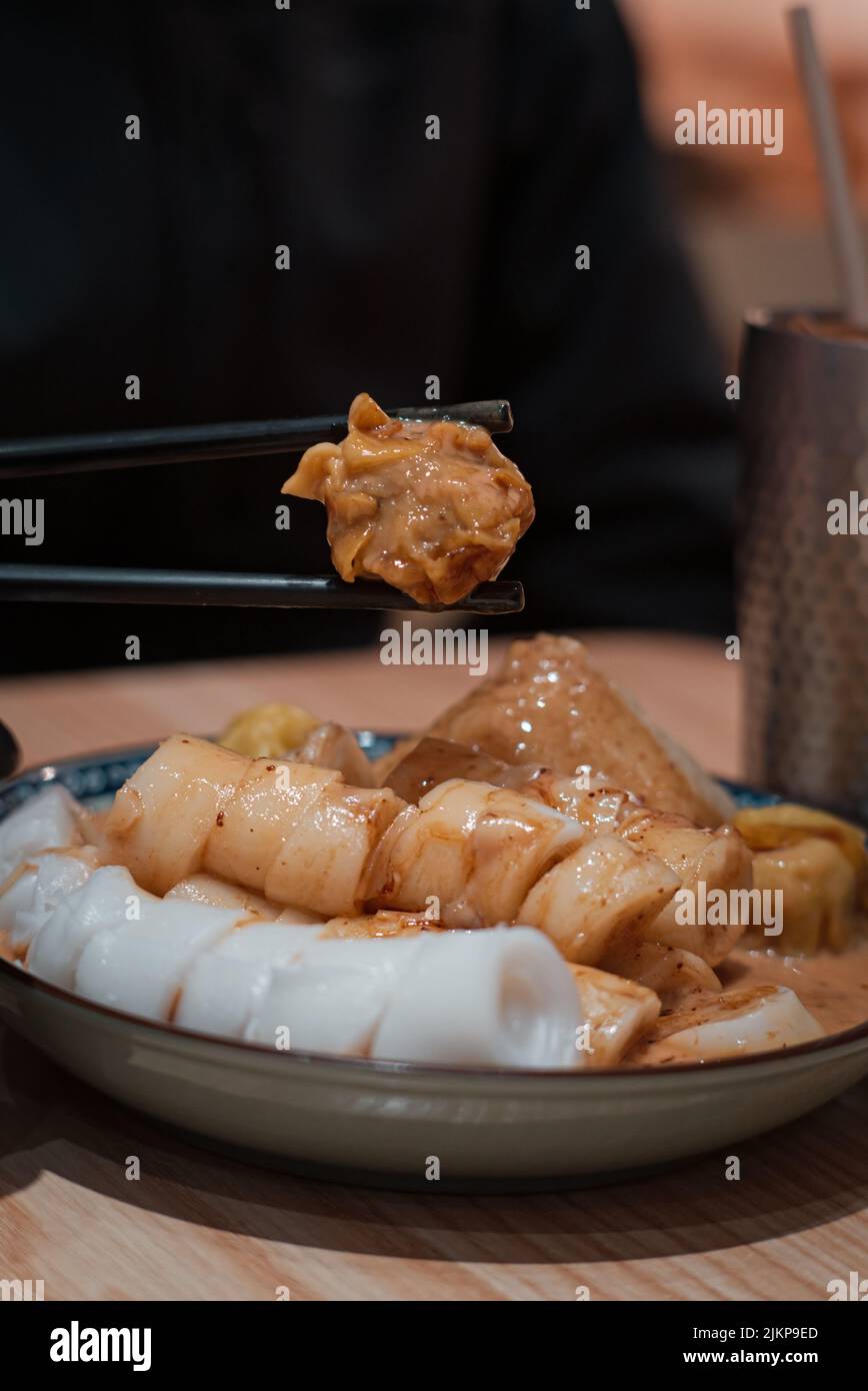 In einem kantonesischen Restaurant in Macau, China, werden in Nahaufnahme Chopsticks mit gedämpften Knödeln und Reisnudelrollen serviert Stockfoto