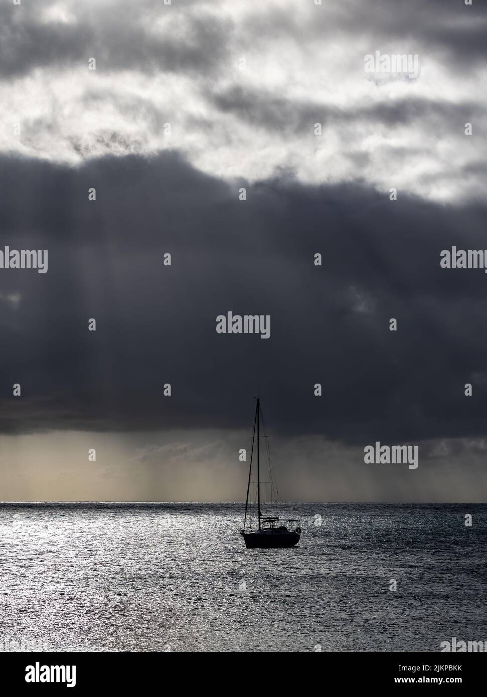 Eine wunderschöne Szene eines silhouettierten Bootes auf dem glänzend grauen Wasser vor einem dramatischen bewölkten Himmel Stockfoto