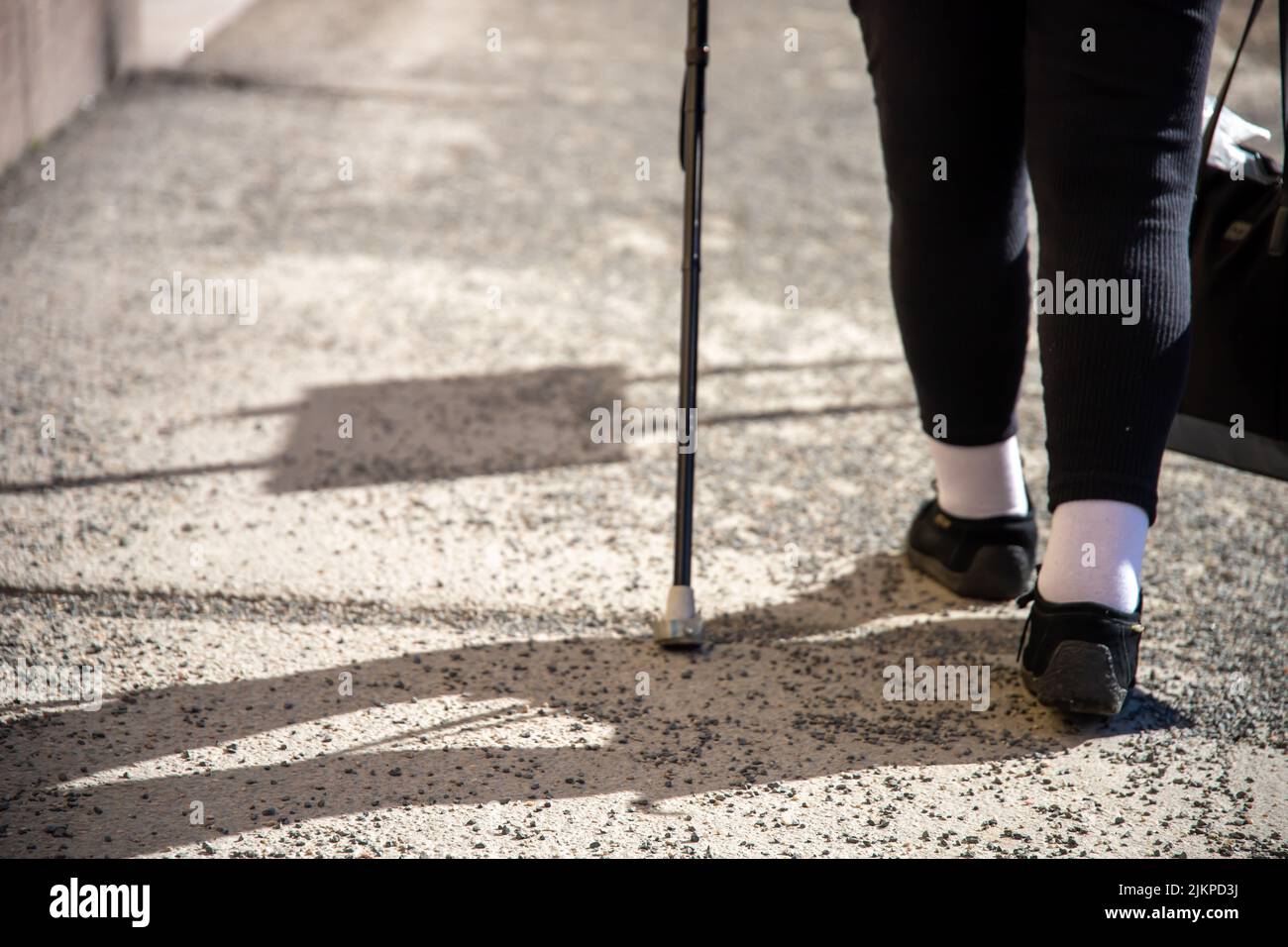 Eine ältere Frau auf der Straße mit einem Stock, ein Schatten auf der Straße.Konzept für Behinderung, Alter, Übergewicht, lahme Person, Beinerkrankungen Stockfoto