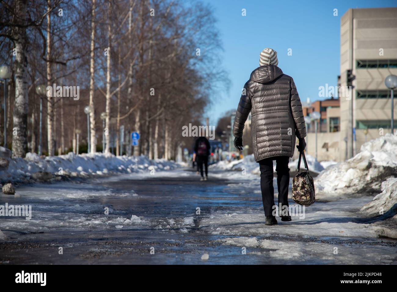 Eine Frau in einer Jacke und einer Tasche in der Hand geht entlang einer verschneiten Straße Stockfoto