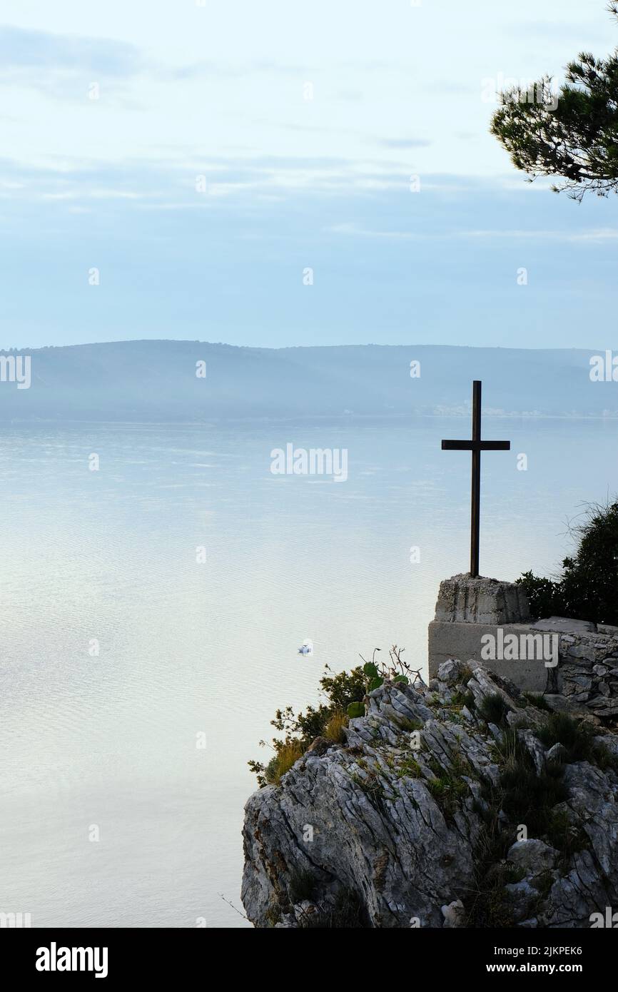 Eine vertikale Aufnahme eines großen Kreuzes auf einer felsigen Klippe im Hintergrund des Ozeans in Kroatien Stockfoto