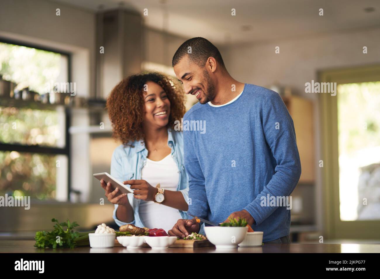 Unser Essen sieht genauso gut aus wie das Rezept. Aufnahme eines glücklichen jungen Paares, das ein digitales Tablet verwendet, während es zu Hause eine gesunde Mahlzeit zubereitet. Stockfoto