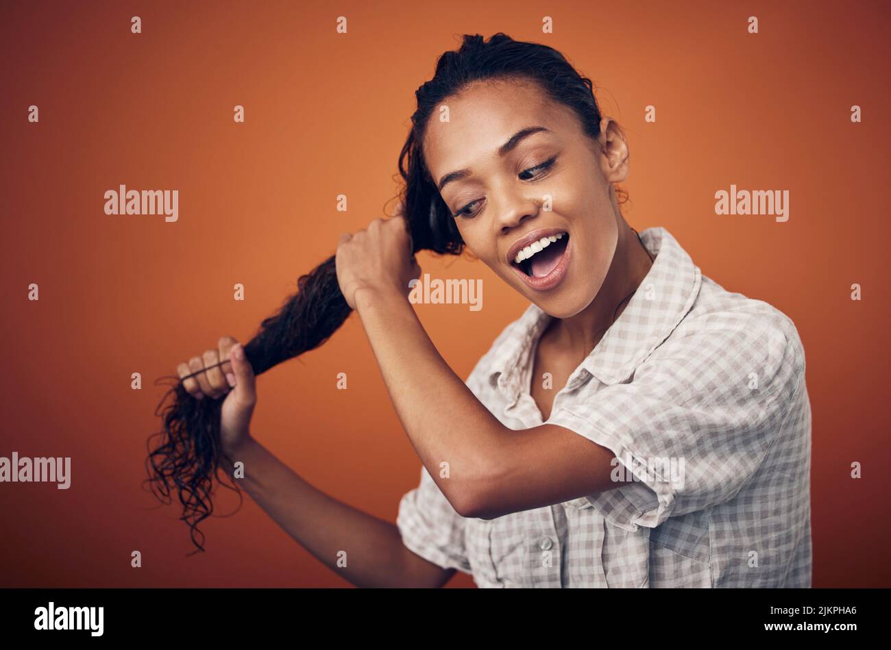 Ich bin dem Erreichen perfekter Locken einen Schritt näher. Eine junge Frau mit nassem Haar posiert vor einem orangen Hintergrund. Stockfoto