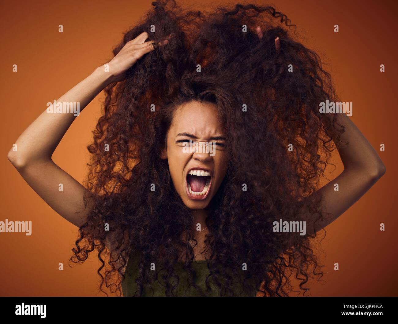 Egal, ich habe nur einen schlechten Haartag. Eine Frau mit lockigen Haaren, die sich frustriert fühlt, während sie vor einem orangen Hintergrund steht. Stockfoto