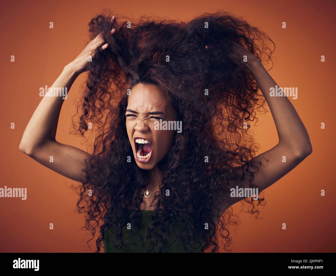 Eine Frau mit lockigen Haaren fühlt sich frustriert, während sie vor einem orangen Hintergrund steht. Stockfoto