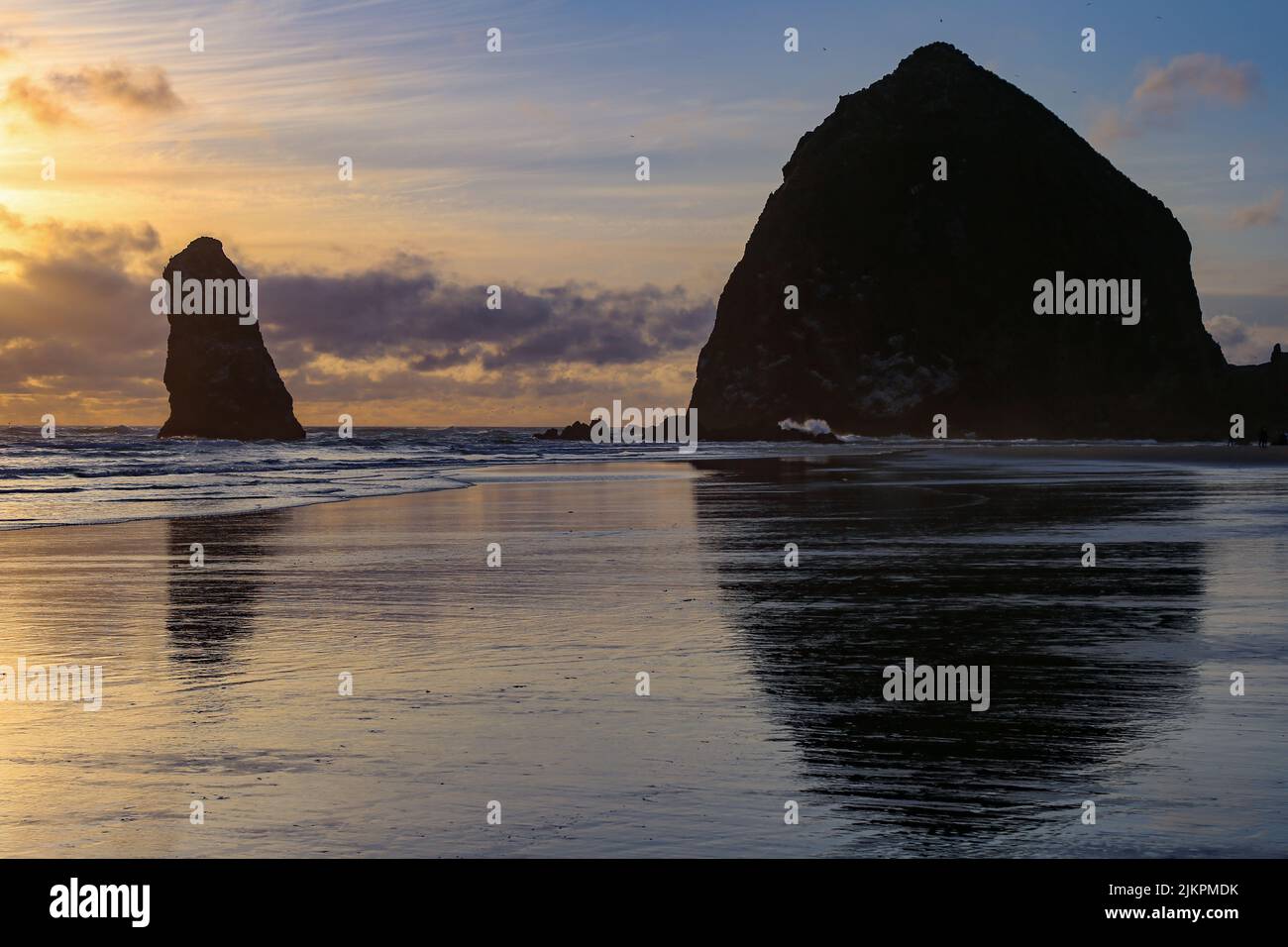 Eine Silhouette des Haystack Rock in Cannon Beach, die sich bei Sonnenaufgang, Oregon, auf der Wasseroberfläche spiegelt Stockfoto