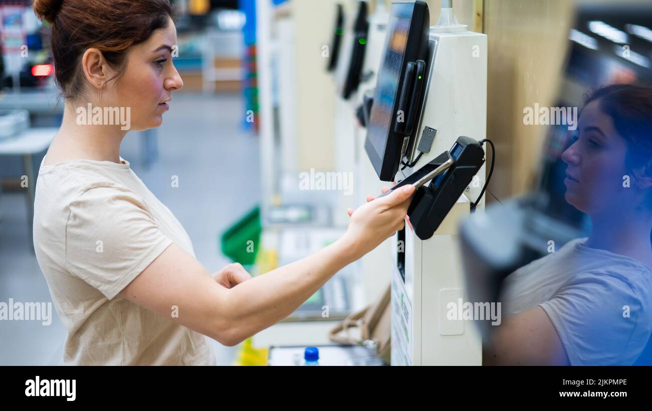 Frau, die mit dem Smartphone im Geschäft am Selbstbedienungsschalter bezahlt. Stockfoto