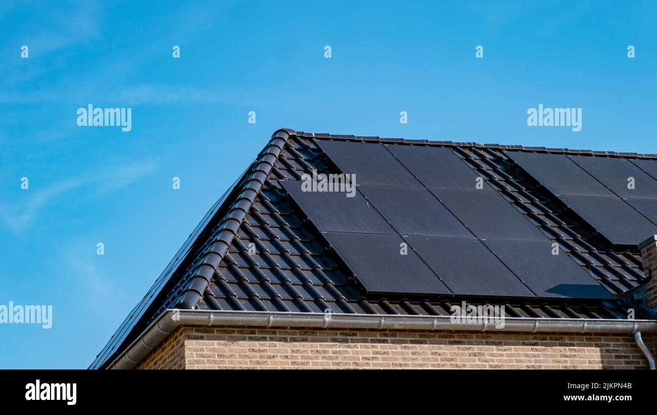 Neubau von Häusern mit Solarpaneelen auf dem Dach vor einem sonnigen Himmel Nahaufnahme eines neuen Gebäudes mit schwarzen Solarpaneelen. Zonnepanelen, Zonne energie, Übersetzung: Sonnenkollektoren, , Sonnenenergie. Stockfoto