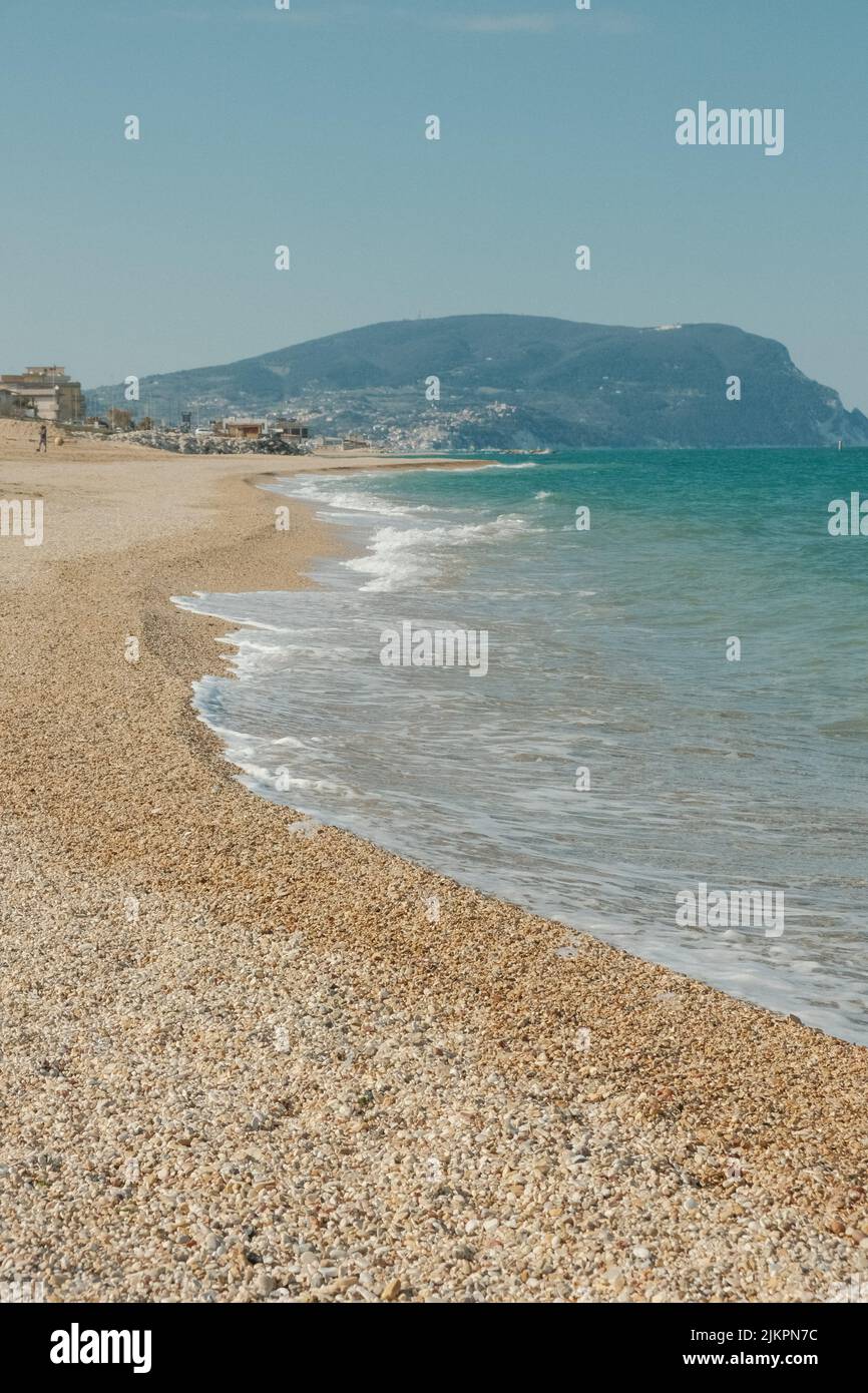 Eine vertikale Aufnahme eines sonnigen Strandes mit kristallklarem Meer, das die Küste wäscht Stockfoto