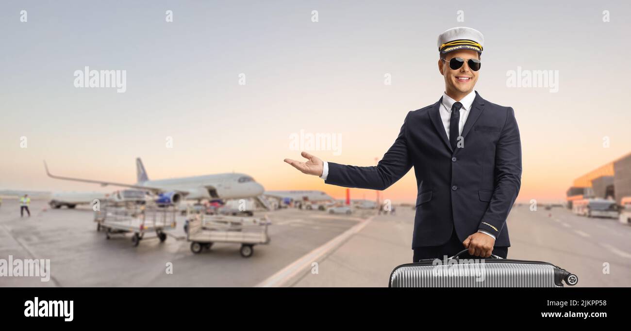 Pilot, der einen Koffer trägt und auf ein Flughafenvorfeld zeigt Stockfoto