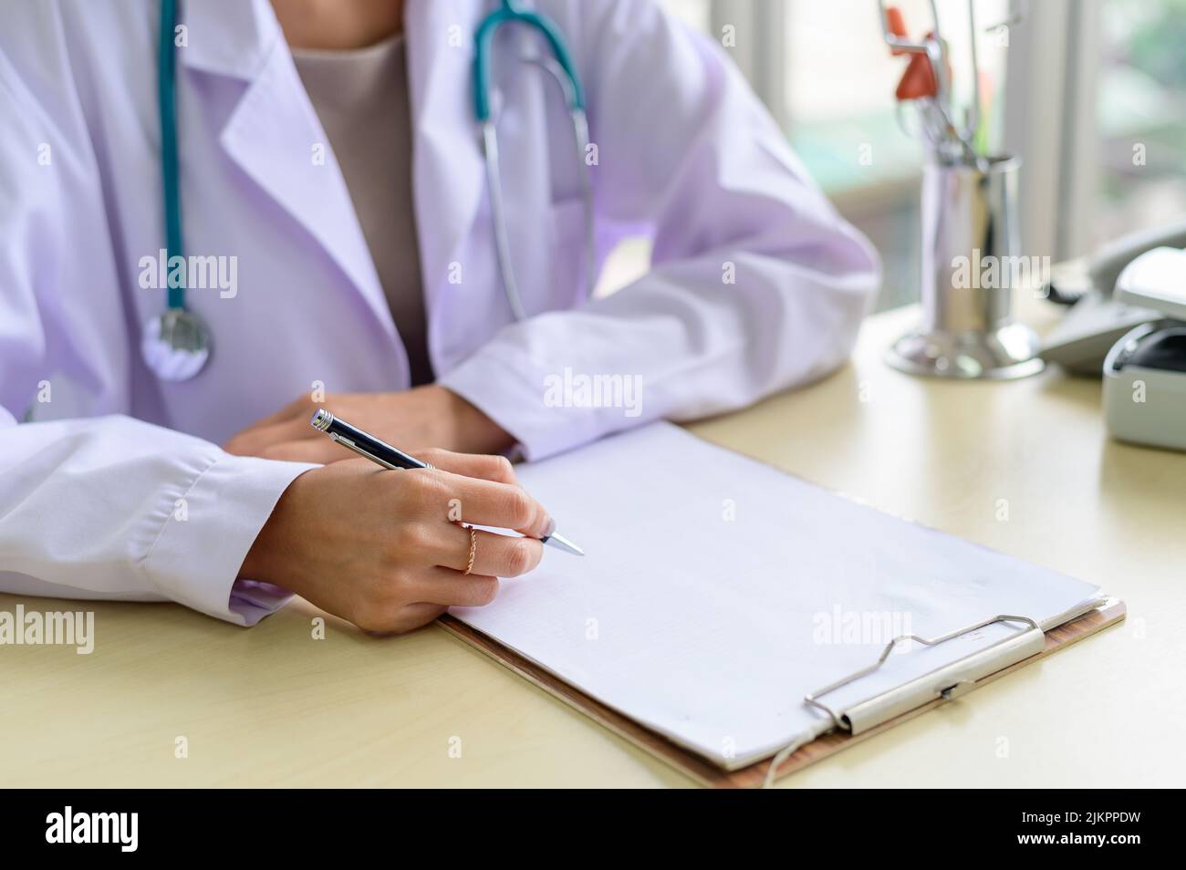 Nahaufnahme eines Arztes, der am Tisch sitzt und Notizen in der Krankenakte macht Stockfoto