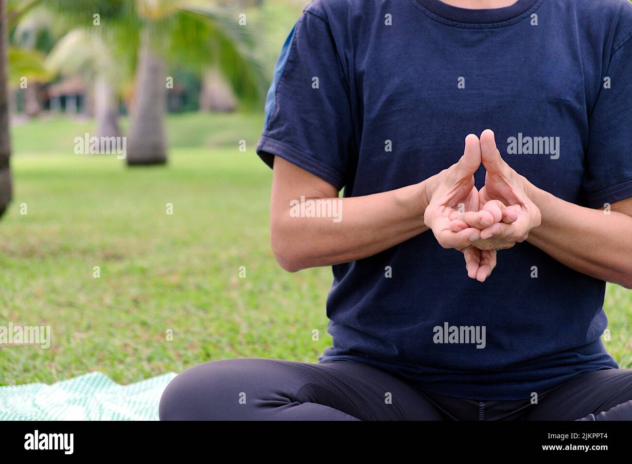 Nahaufnahme eines Halbkörpers einer asiatischen Frau, die morgens auf dem öffentlichen Park Yoga-Übungen mit der Haltung der Finger macht Stockfoto