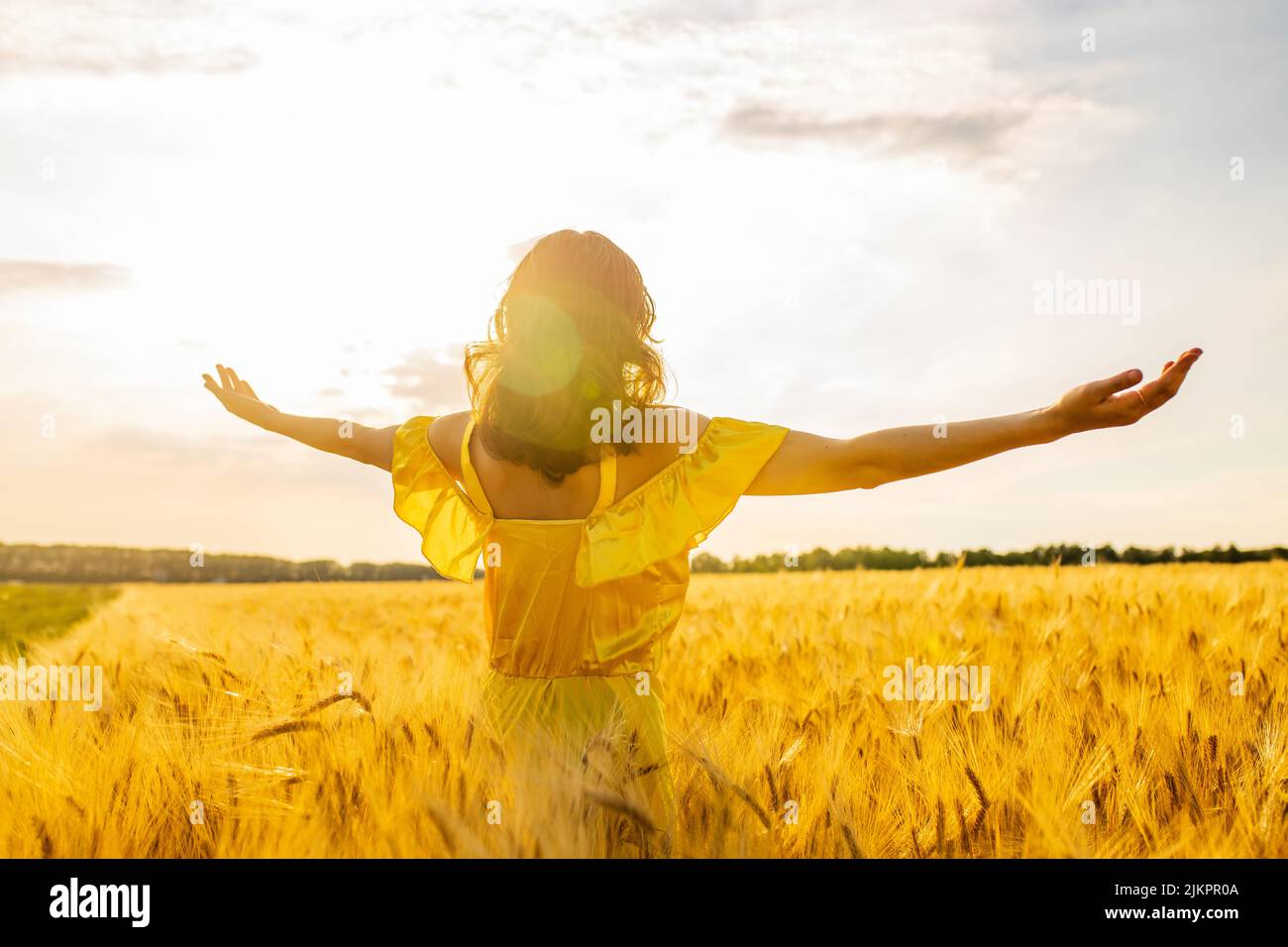 Junge Frau in gelbem Kleid auf einem Weizenfeld mit Sonnenaufgang im Hintergrund Stockfoto