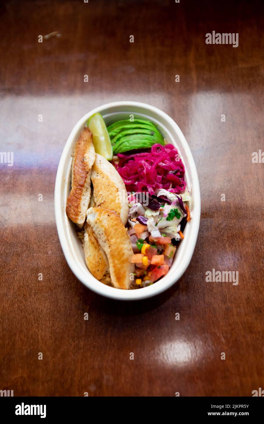 Ein Blick von oben auf eine mexikanische Fischschale mit Guacamole, Rettich, Reis und Gemüse auf einem schwarzen Tisch Stockfoto