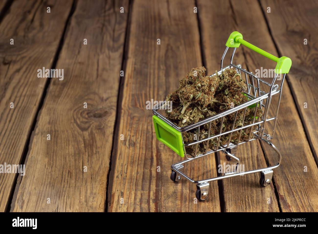 Getrocknete Marihuana-Knospen liegen in einem Einkaufswagen auf Rädern auf einem hölzernen Hintergrund Stockfoto