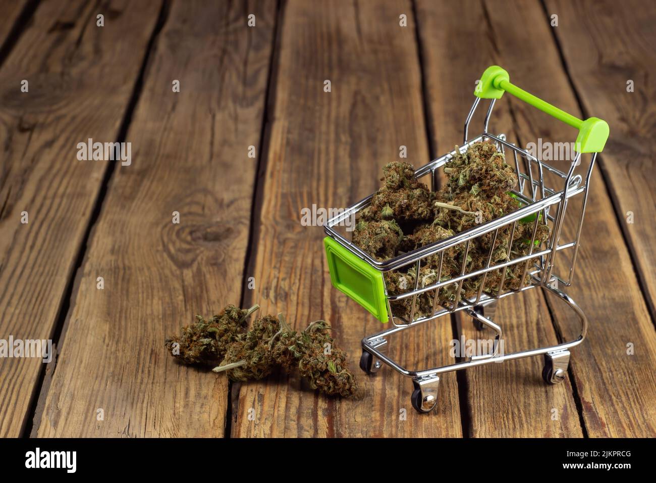 Getrocknete Marihuana-Knospen liegen in einem Einkaufswagen auf Rädern auf einem hölzernen Hintergrund Stockfoto