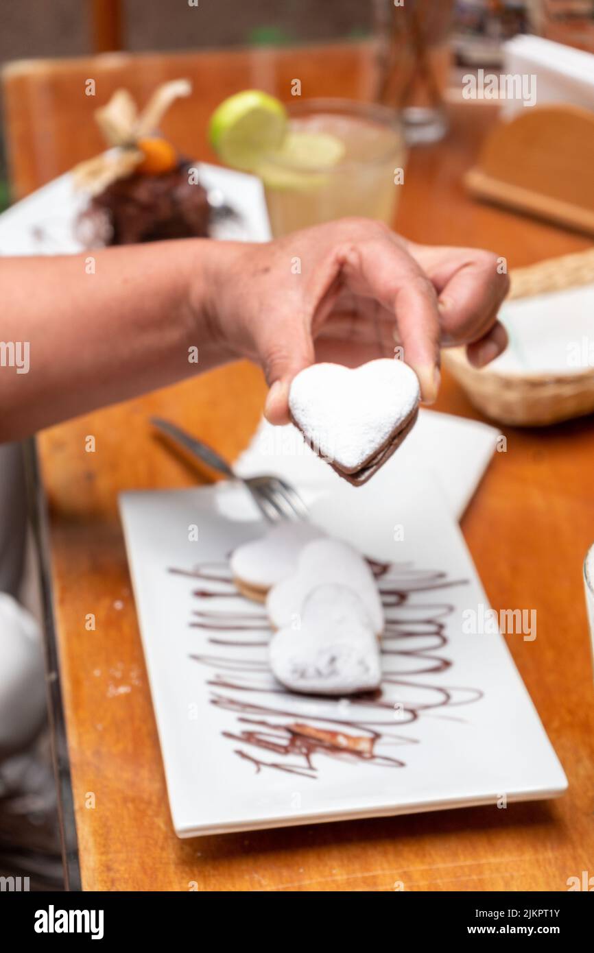 Ein selektiver Fokus auf eine Hand, die ein herzförmiges Gebäck hält, das in einem Restaurant serviert wird Stockfoto