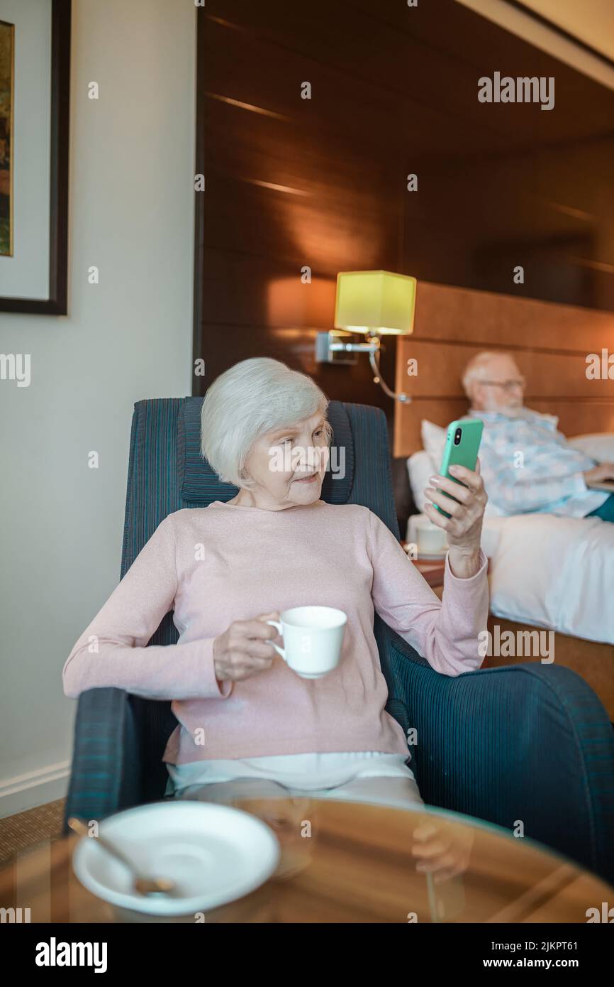 Ältere gut aussehende Dame mit Kaffee und hoding ein Smartphone in den Händen Stockfoto