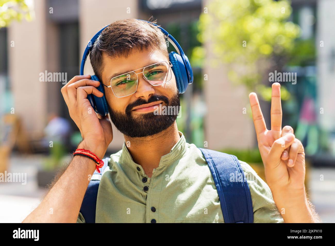 indischer Student mit blauem Headset und Rucksack, der an einem sonnigen Tag gut aussieht Stockfoto