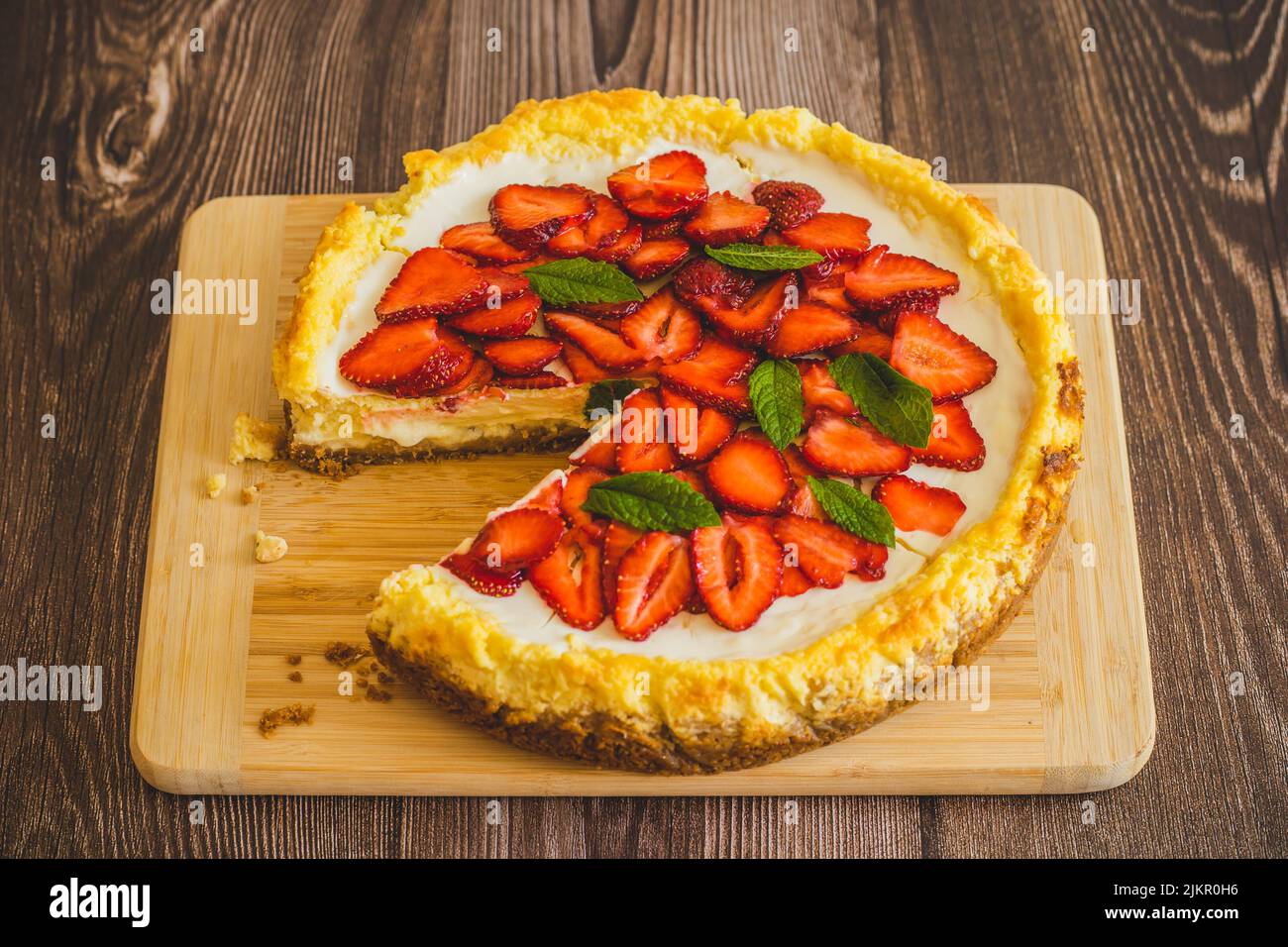 Stück Erdbeer hausgemachten Kuchen auf Holztisch.köstliche Käsekuchen mit Erdbeeren mit Minzblättern verziert.Draufsicht.gesunde Bio-Sommer werden Stockfoto