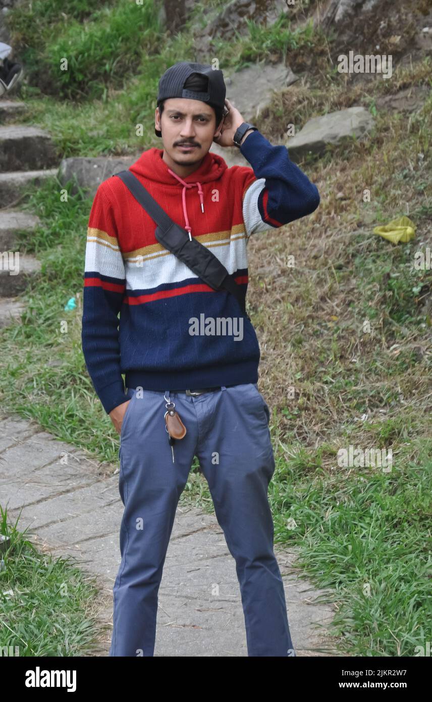 Vorderansicht eines jungen indischen Mannes mit Mütze nach hinten, der im Freien mit einer Hand in der Tasche auf die Kamera schaute Stockfoto