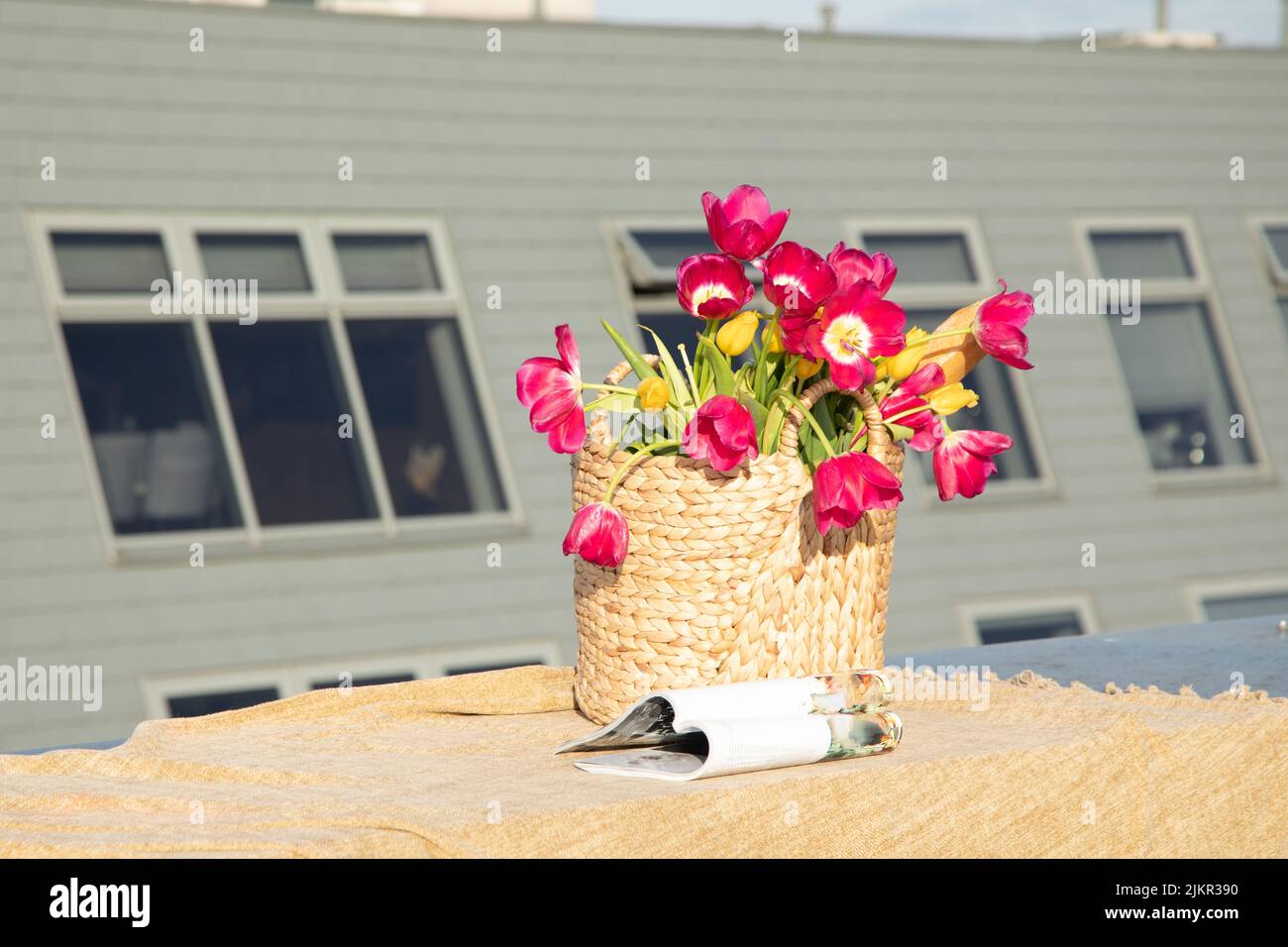 Großer Korbkorb mit frischen blühenden rosa Tulpen und Modezeitschrift auf dem Dach des Hauses, Drehort mit Beauty-Dekor. Pariser Stil, Romantik Stockfoto