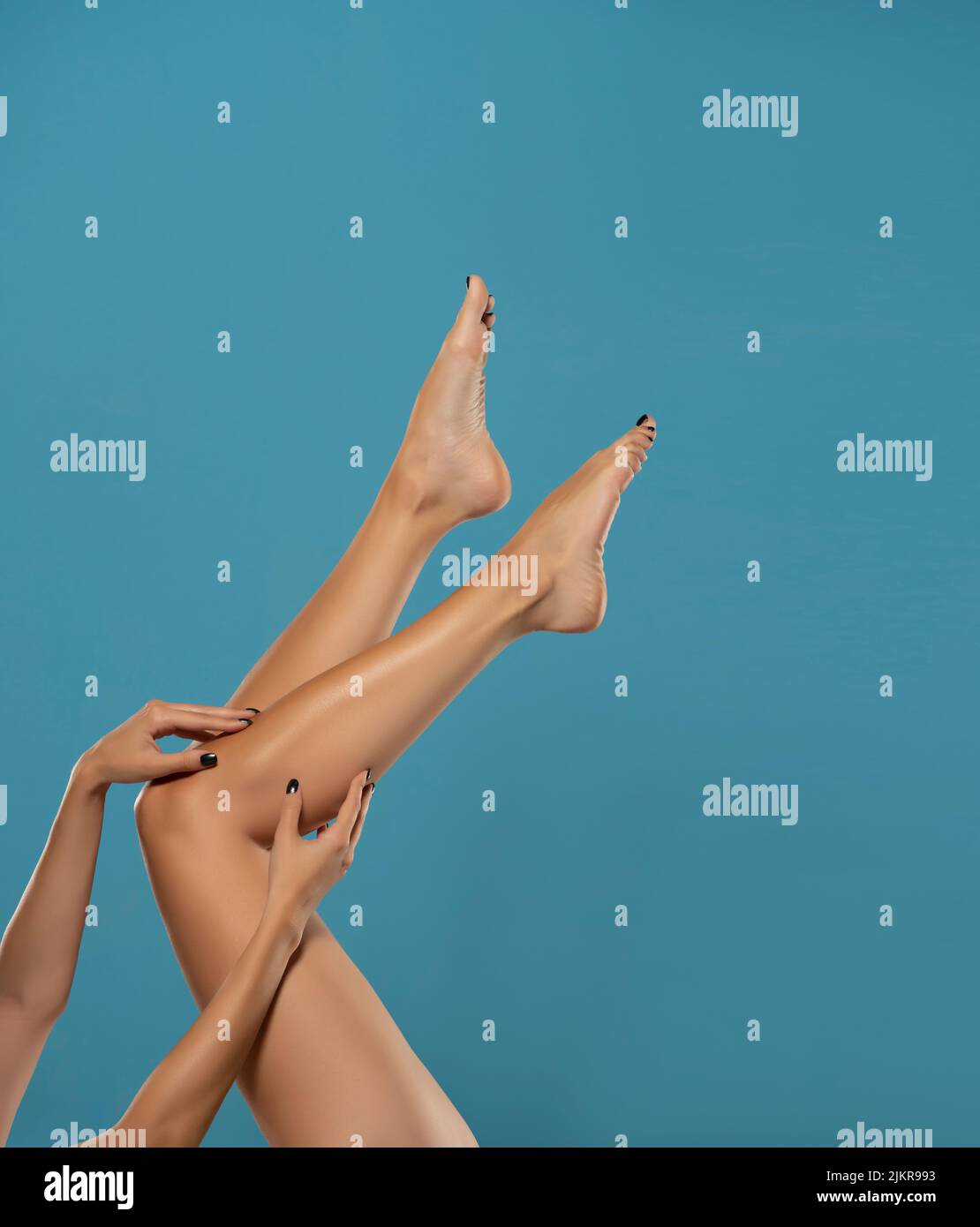 Junge Frau berührt ihre glatten langen Beine nach der Rasur auf blauem Hintergrund. Stockfoto